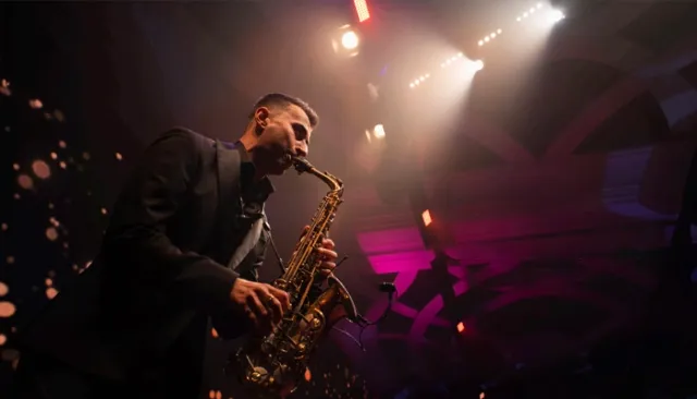 Saxophonist performing beneath stage lights at an event